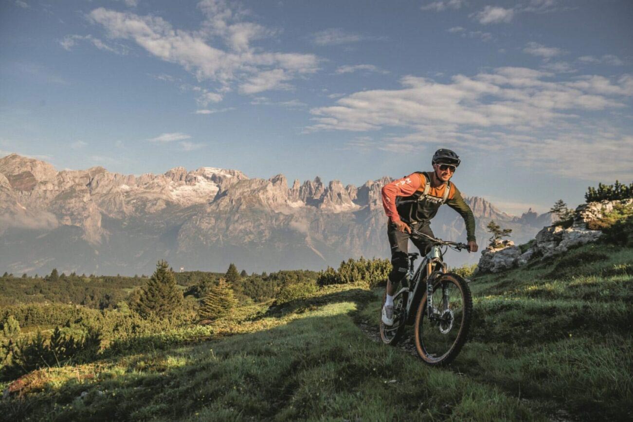 Ein sportlicher Mann mit Radhelm lächelt beim Mountainbiken durch grüne Landschaft