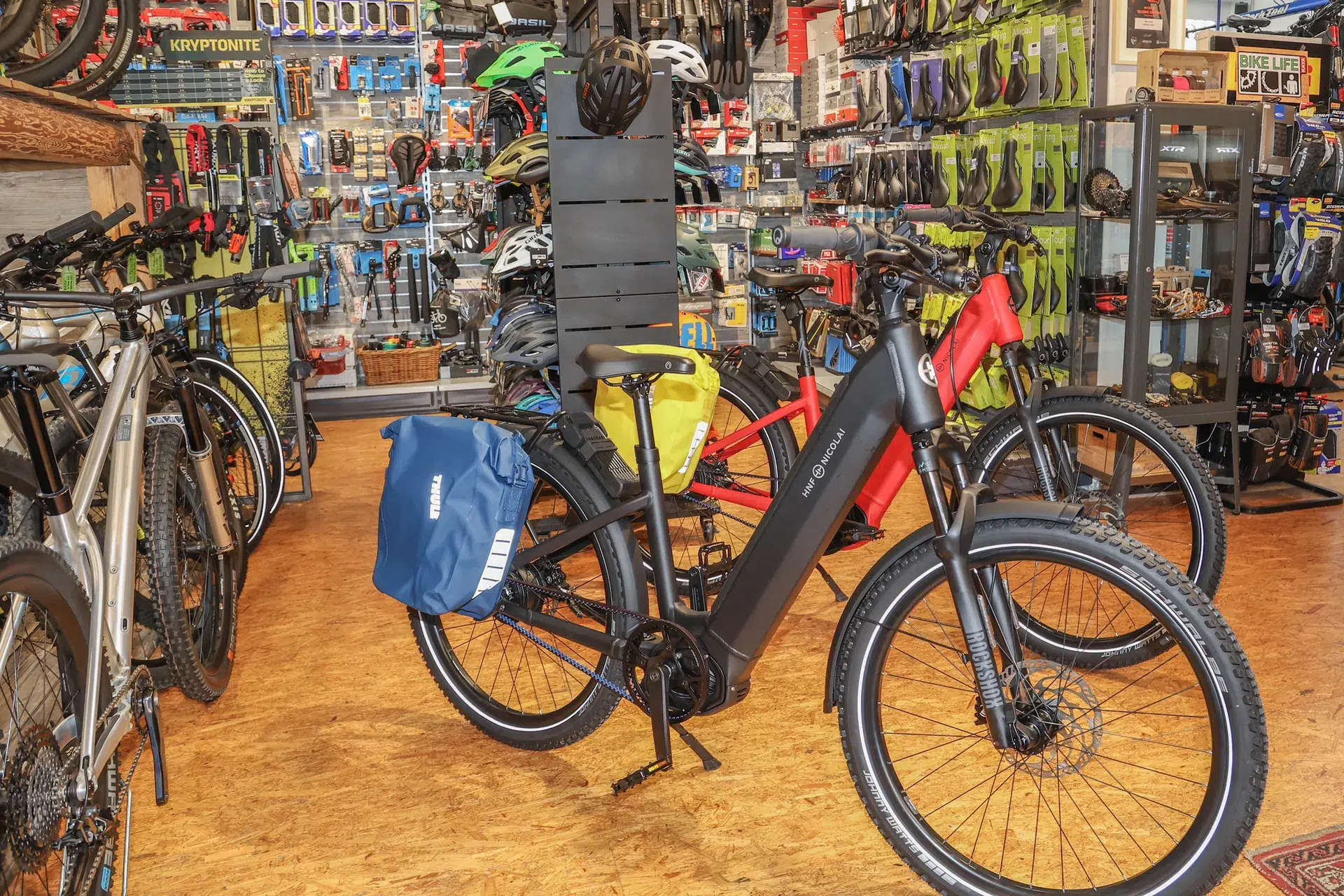 Ein schwarzes E Bike mit blauen und gelben Packtaschen steht in einem Fahrradladen