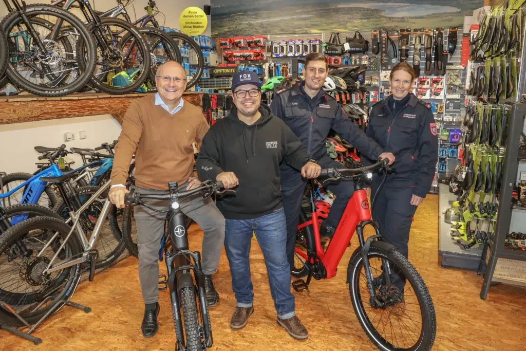Vier freundlich lachende Erwachsene stehen mit modernen Fahrrädern in einem Fahrradladen